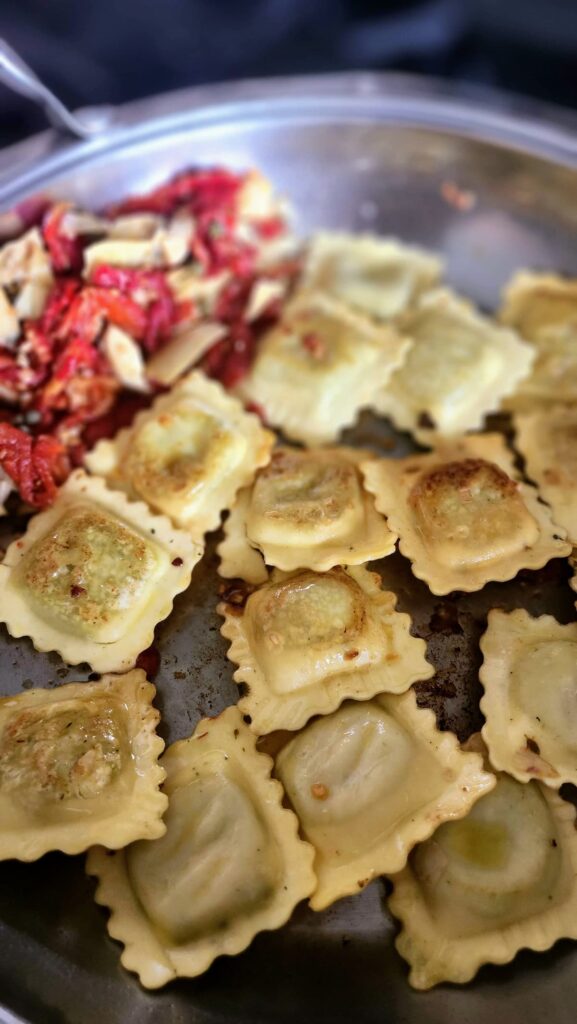 sauteed ravioli in frying pan with sundried tomatoes, artichokes and capers pushed to side