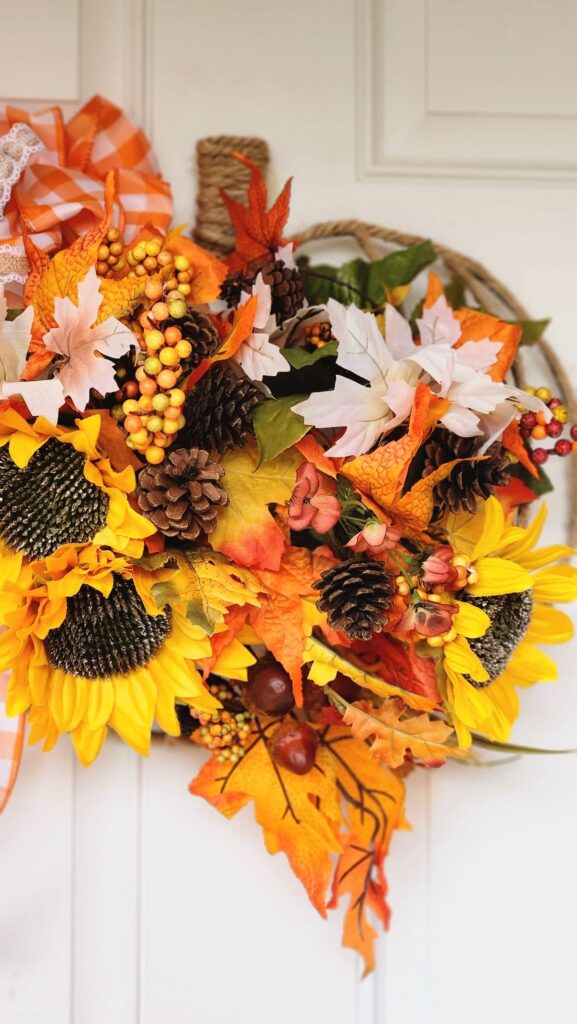 diy wire pumpkin wreath with orange bow and flowers hanging on front door