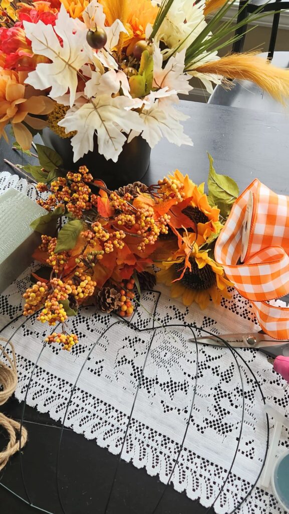 faux flowers, wire pumpkin wreath and suppllies on table to make a wreath