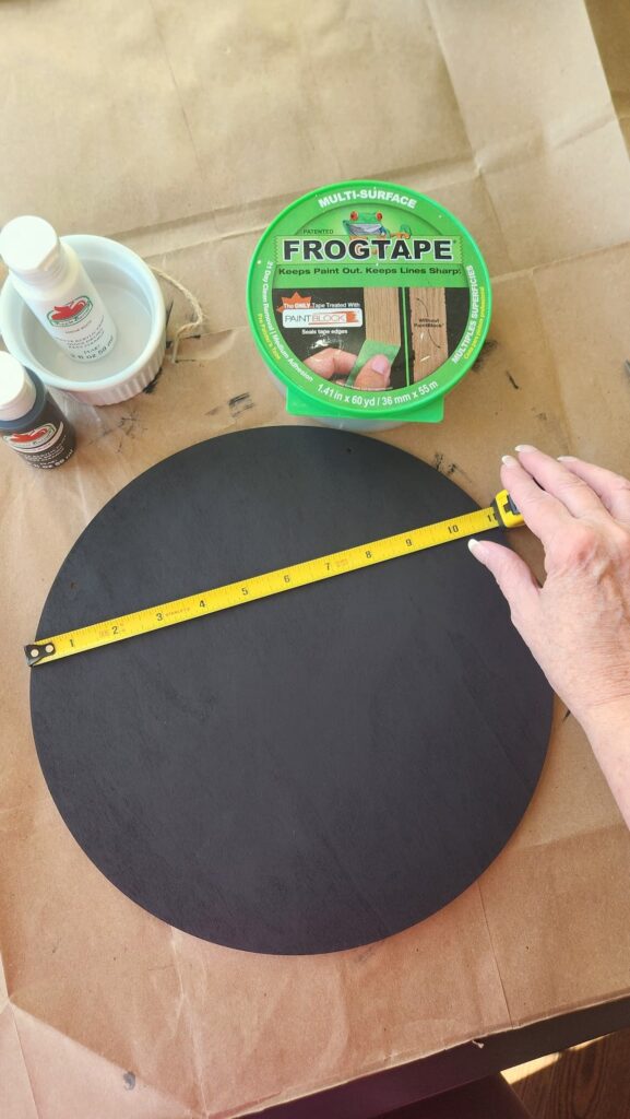 painted round wooden door hanger with measure tape across marking the inches for stripes to be painted