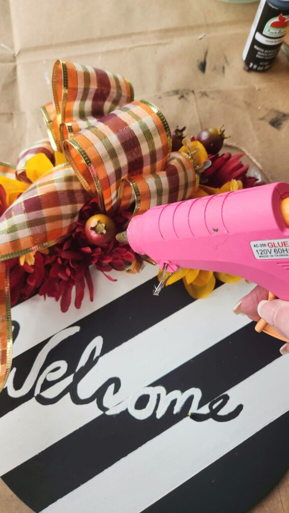 fall faux flowers being glued to diy door hanger with glue gun