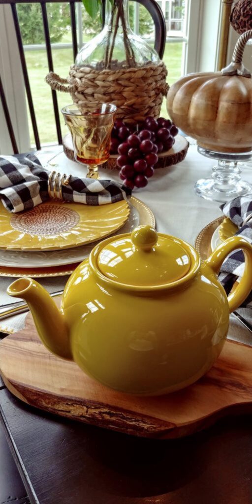 yellow teapot on table with wooden grapes and sunflower dishes
