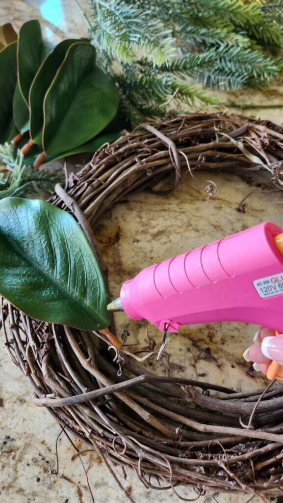 pink blue gun adding magnolia leaves one at a time to grapevine wreath