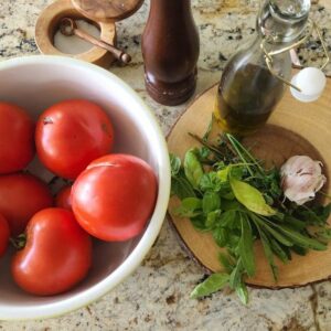 fresh tomatoes in bowl on counter with herbs on side