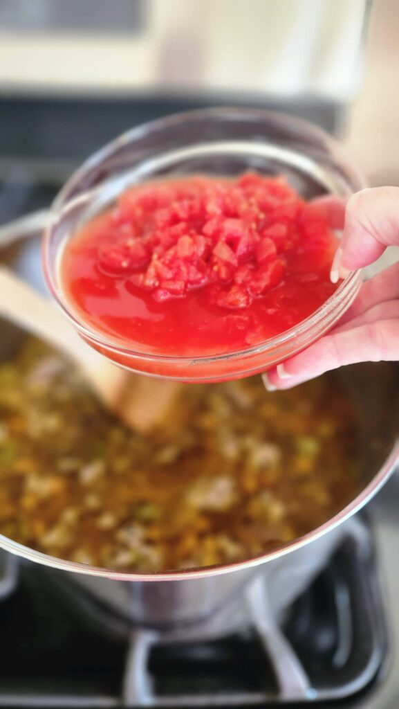 diced tomatoes in glass bowl being poured into stock pot of holiday hash
