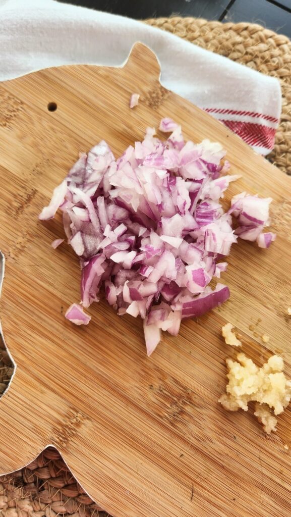 piggy shaped cutting board with diced onions and minced garlic on it
