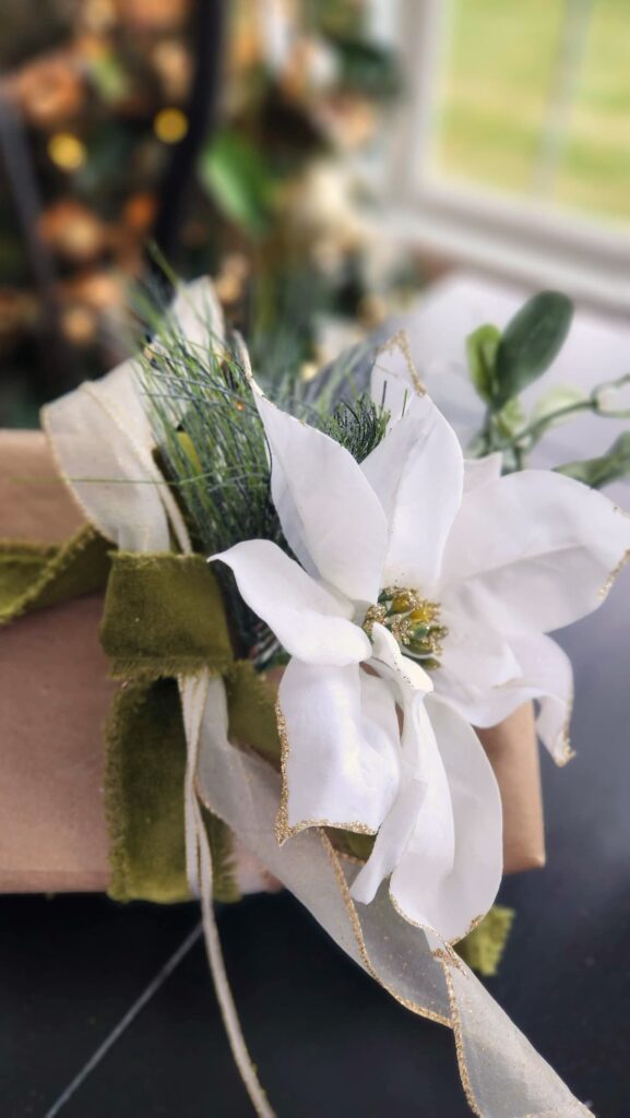 white faux poinsettia on a brown package tied with ribbon on table