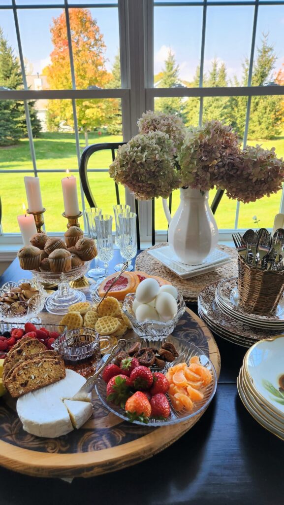 kitchen table with a breakfast charcuterie board on it with hard boiled eggs, mini muffins, mini waffles, frut and nuts