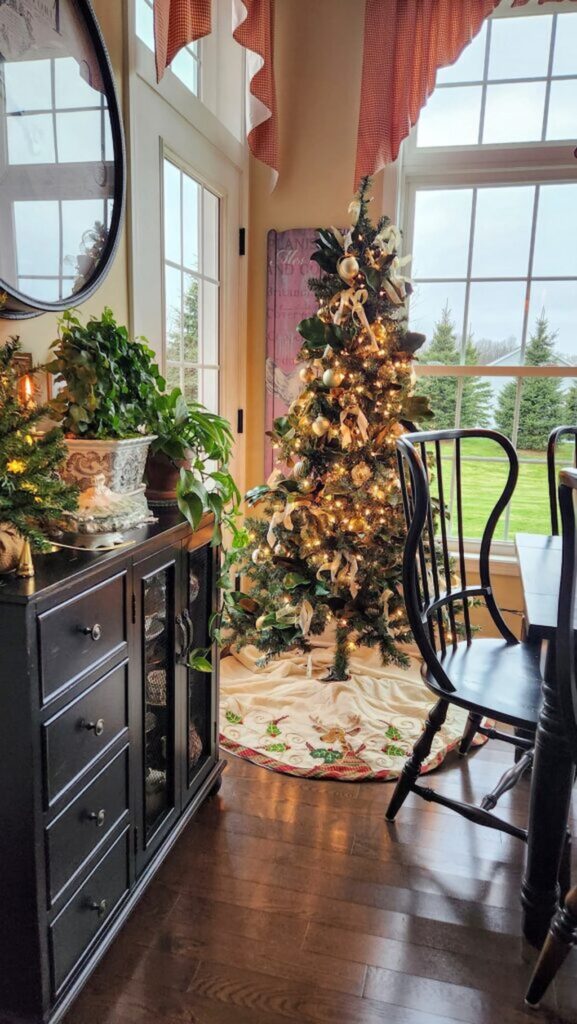 christmas tree lit up in breakfast room with gold ornaments on it