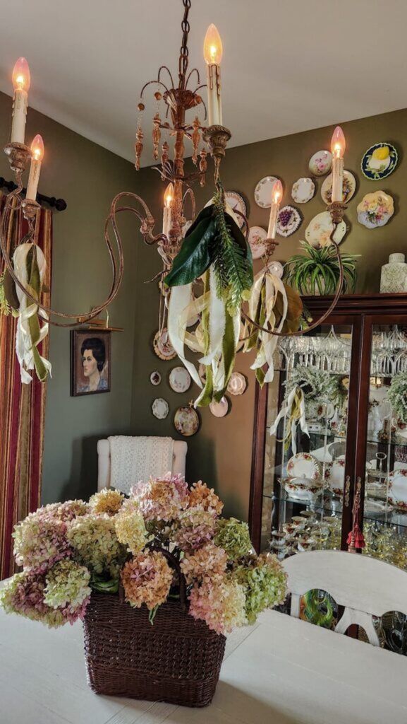 dining room table with basket of dried hydrangeas and chandelier with green and ivory velvet ribbons hanging from the light