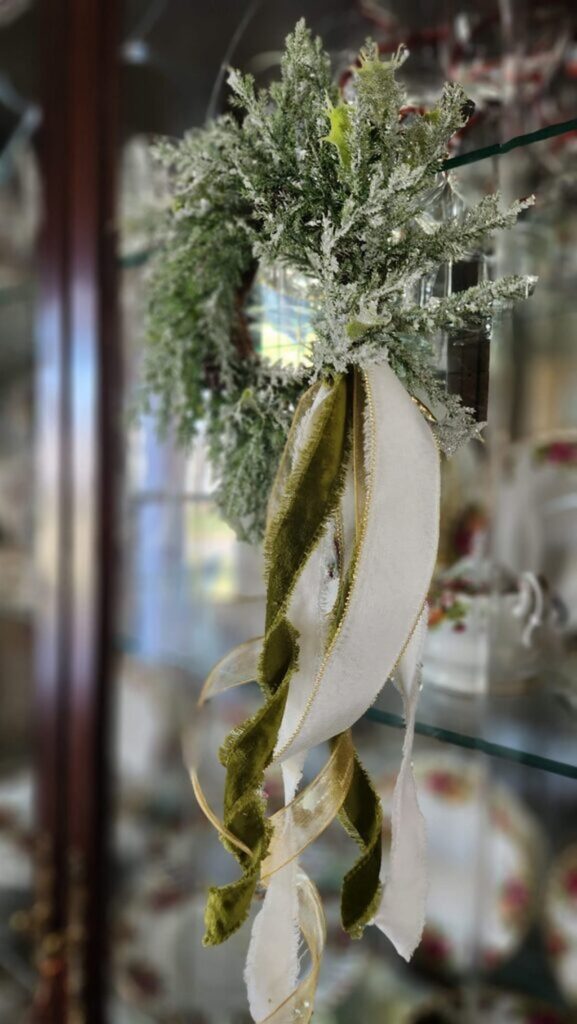 green small wreath with silver accents hung on glass curio door with velvet ribbon hanging down