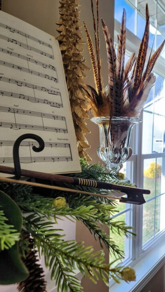 violin bow and glass vintage vase holding pheasant feathers on christmas mantel