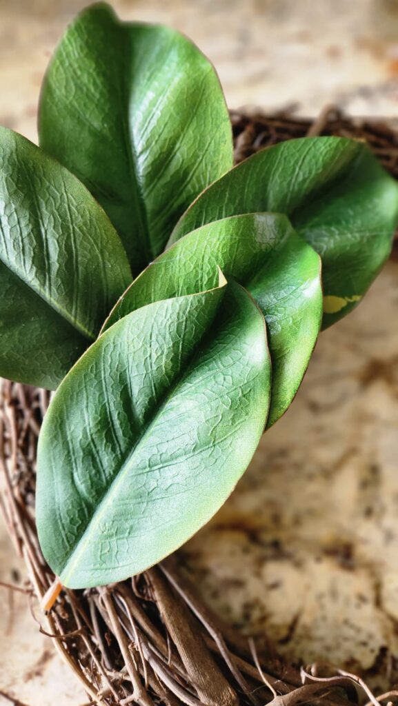 faux magnolia leaves being added with hot glue to the wreath base