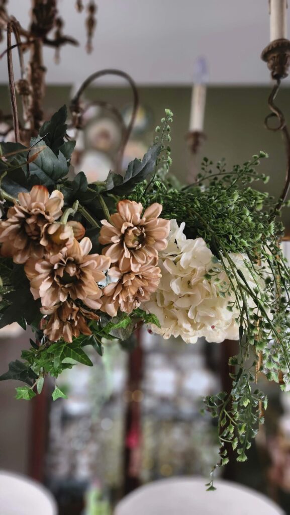 brown and ivory faux florals hanging from chandelier with greenery cascading down