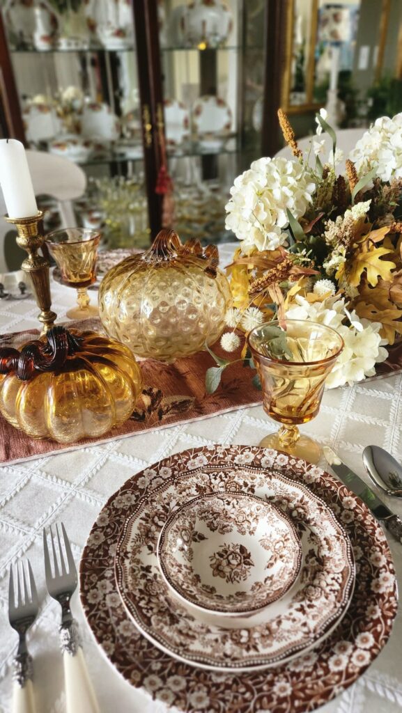 amber glass pumpkins, amber stemware, brown chintz dishes and fall florals on table 