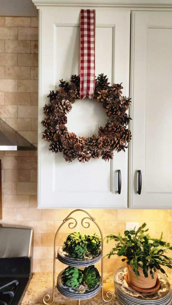 pinecone wreath hanging from burgandy checked ribbon on kitchen cabinet door