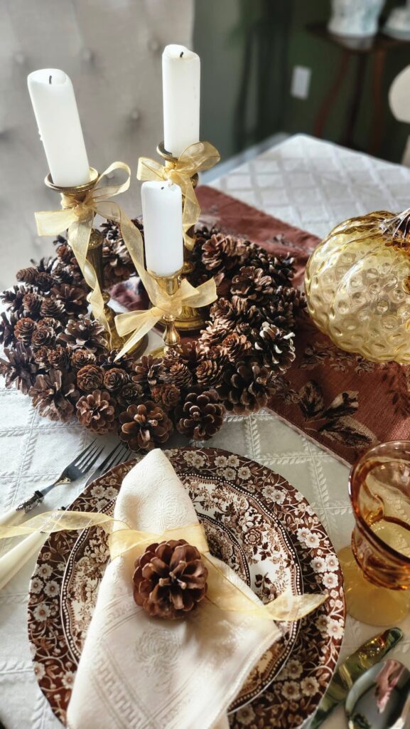 finished pine cone wreath on table with three brass candlesticks and candles in the middle of the wreath