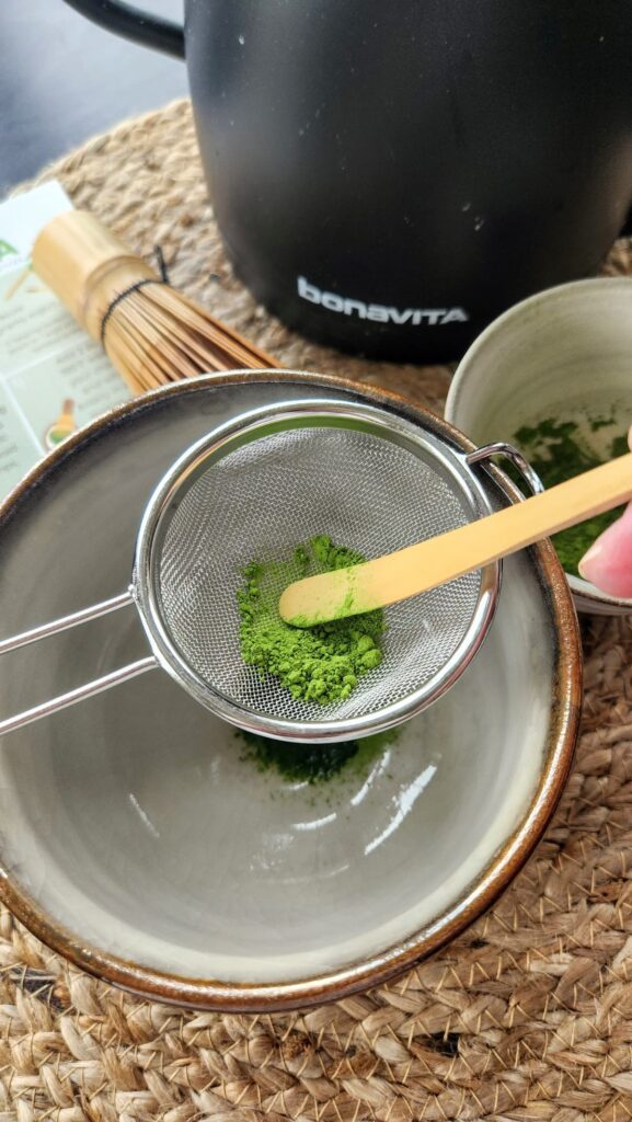pushing the matcha thru the strainer withthe wooden scoop