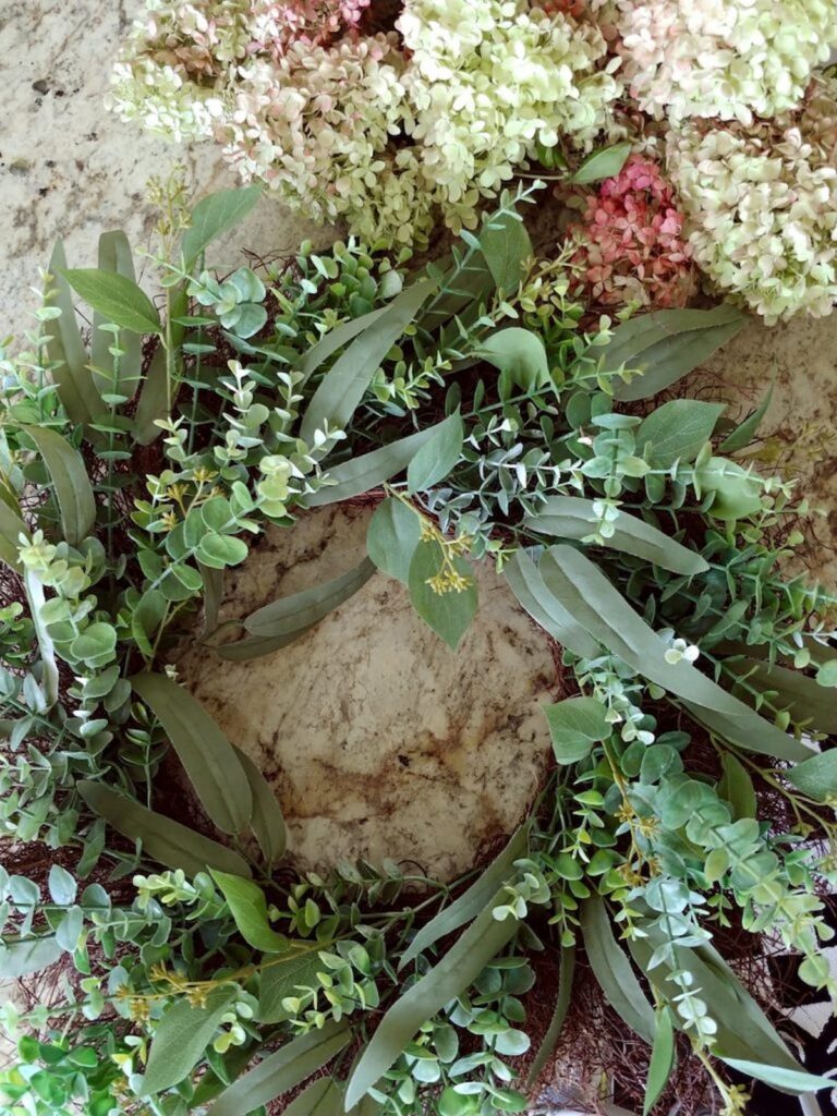overhead view of wreath with hydrangeas being added to the greenery