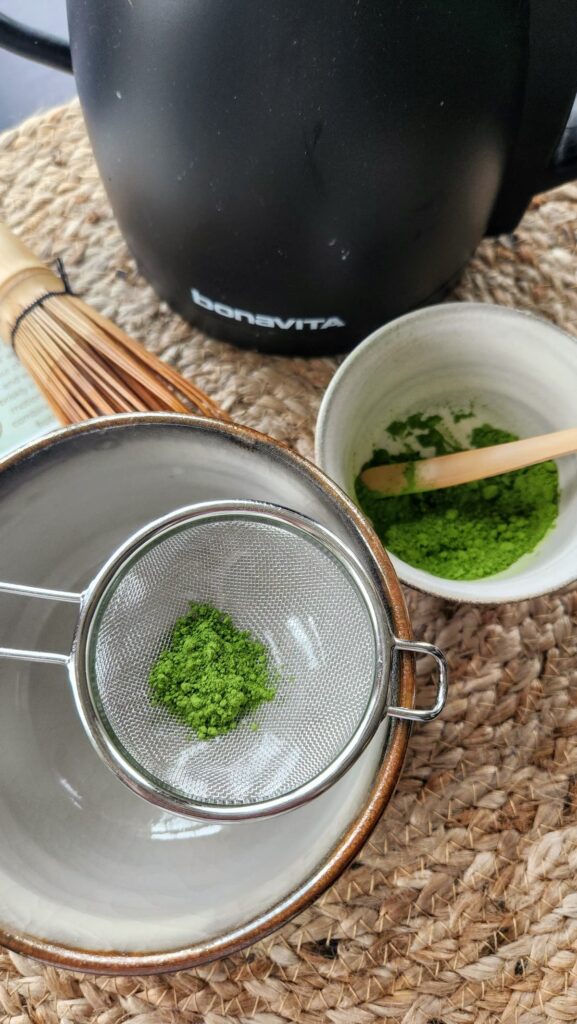 matcha being added to the stainless steel strainer prior to whisking