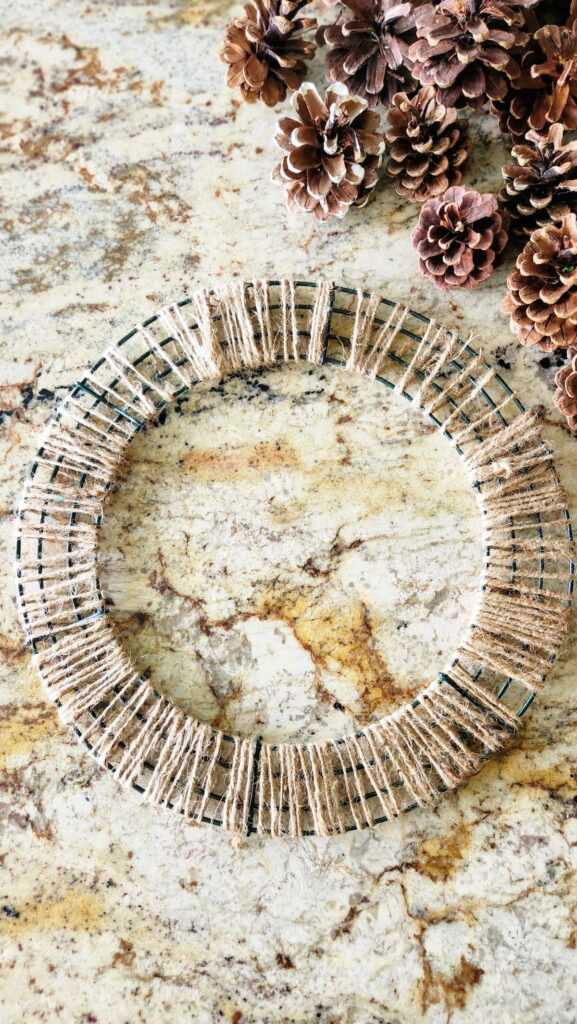 overhead view of wreath form wrapped with jute twine and pinecones on counter