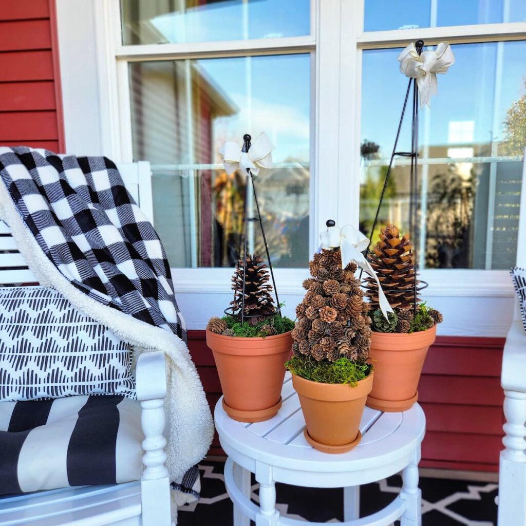 three diy outdoor pinecone topiaries on white porch table on front porch