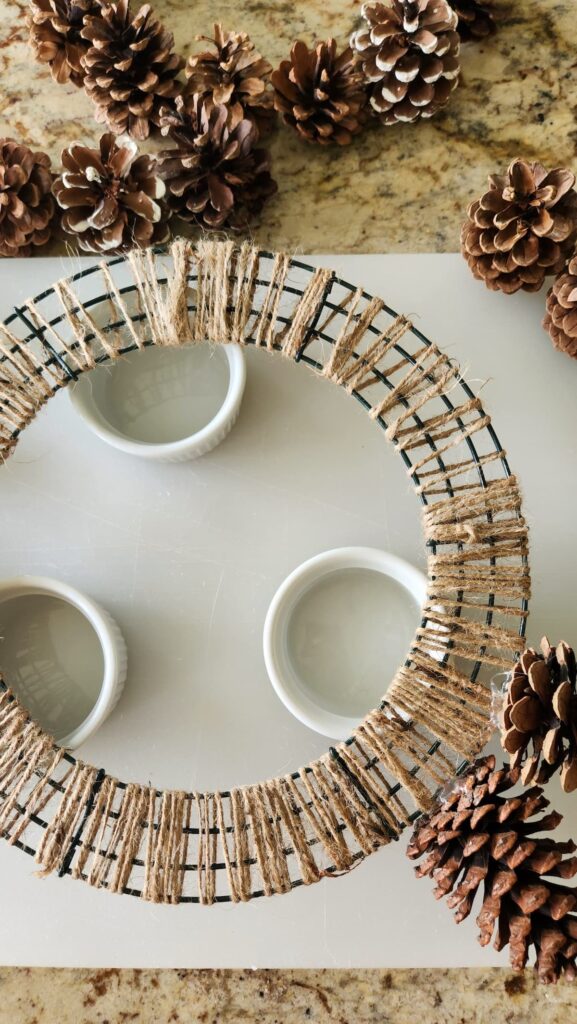 wire form with jute twine elevated on counter with three white ramekin bowls getting ready to add pinecones