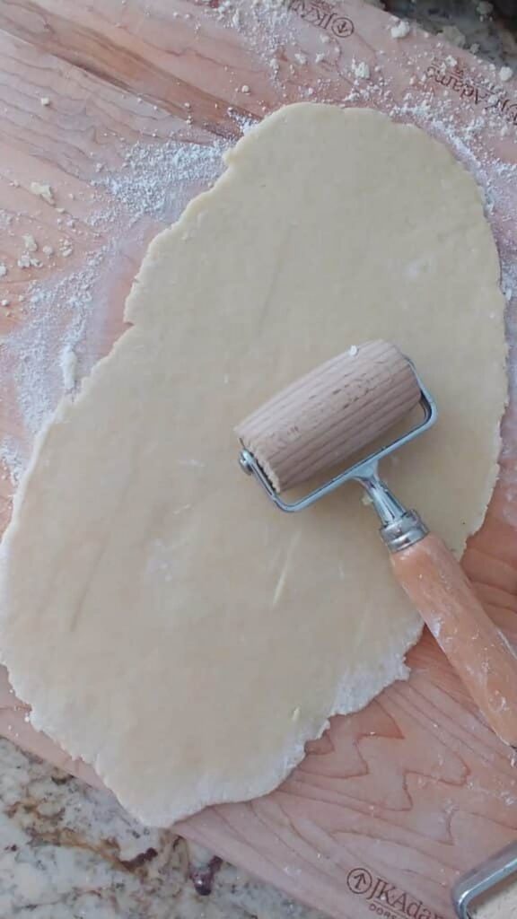 dough being rolled out on wooden board for cherry tarts