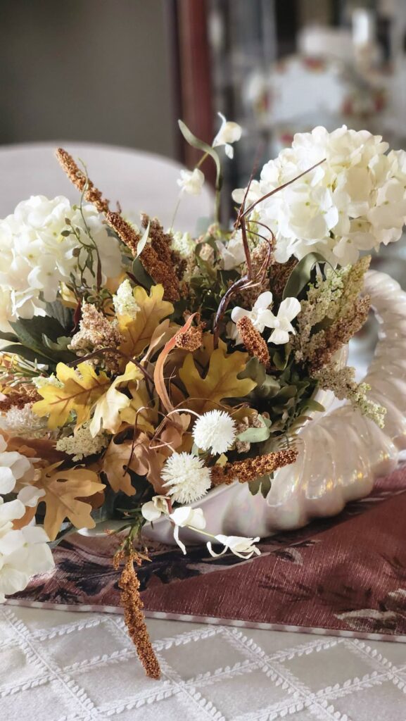 ivory ceramic cornacopia with brown and tan and ivory faux floral arrangement in it