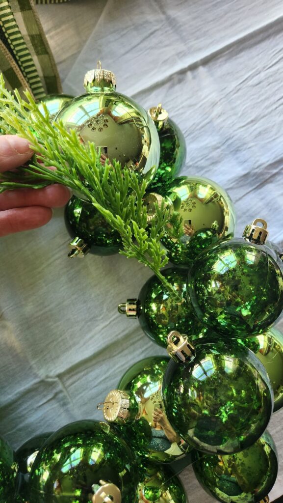 adding faux greenery to the wreath form in between the ornament bulbs