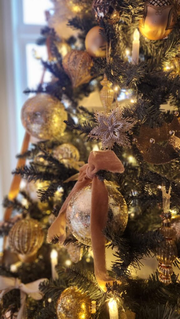 gold ornaments on christmas tree with gold velvet bows tied at the top of the ornament