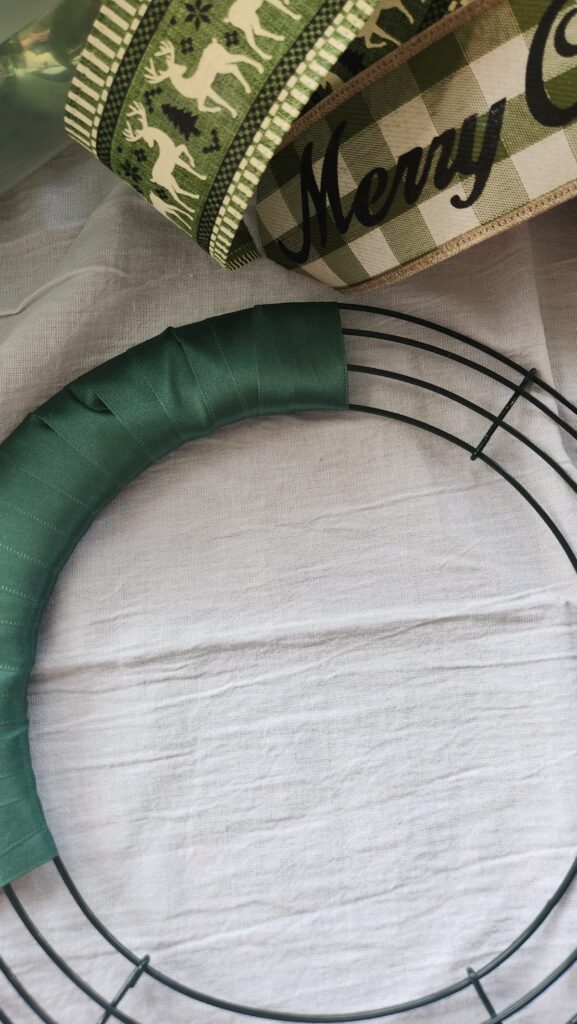 wire wreath form with green ribbon being wrapped around the wire form