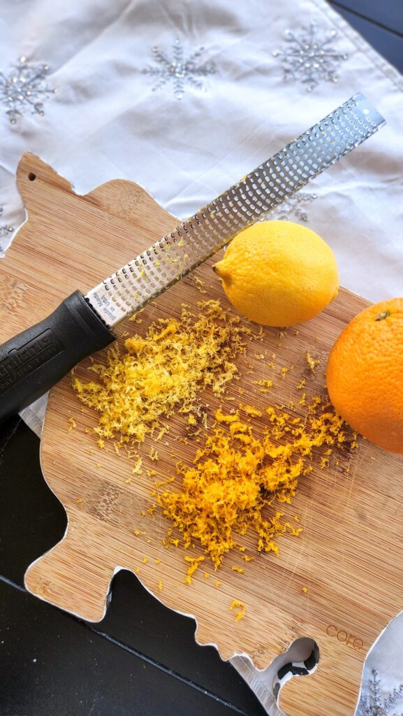 wooden cutting board with a lemon and orange being zested