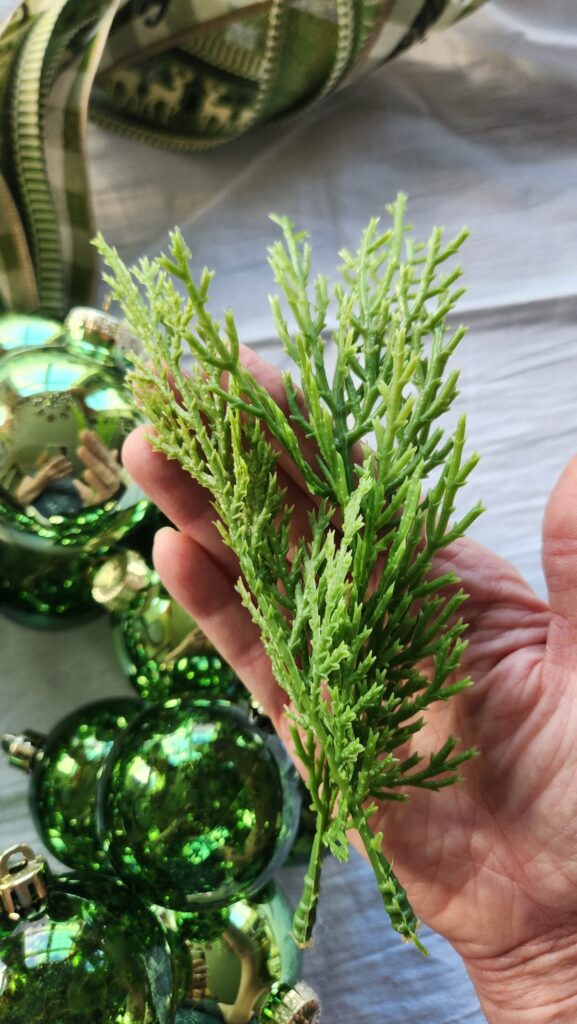 adding faux cedar greenery to the small empty spaces of the wreath