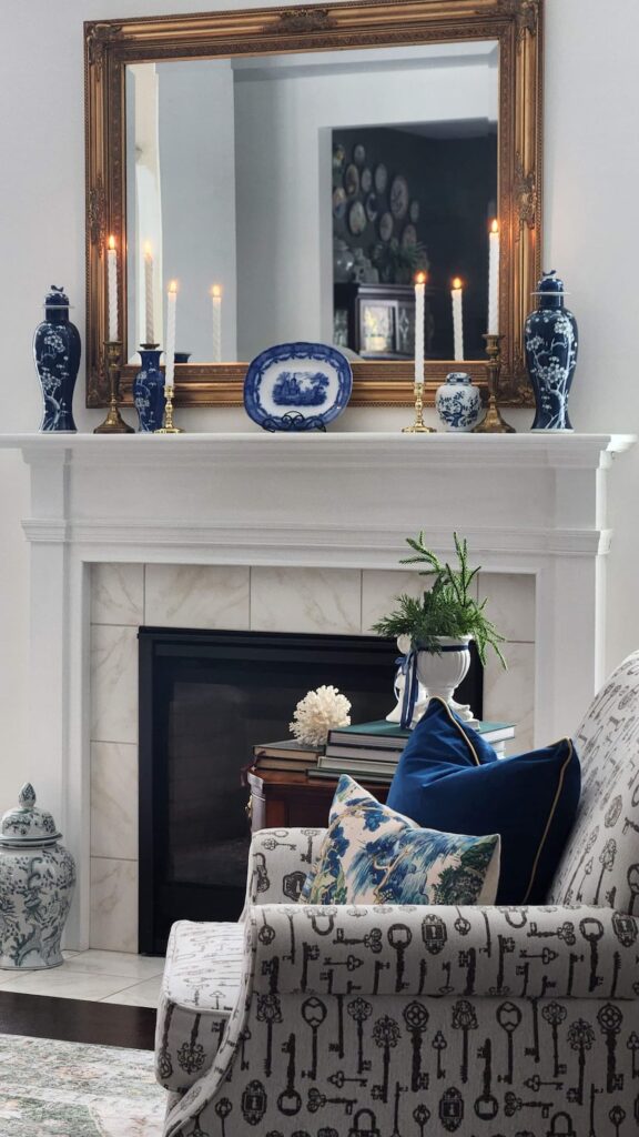 mantel with blue and white vintage items on it and blue pillows on chair by fireplace