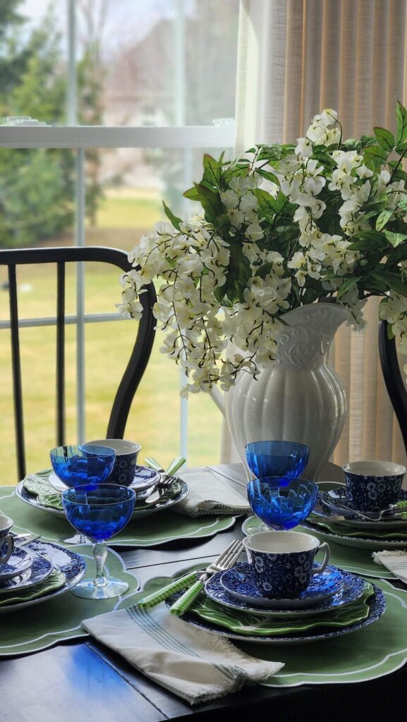 white pitcher filled with white wisteria's on table with mismatched dishes