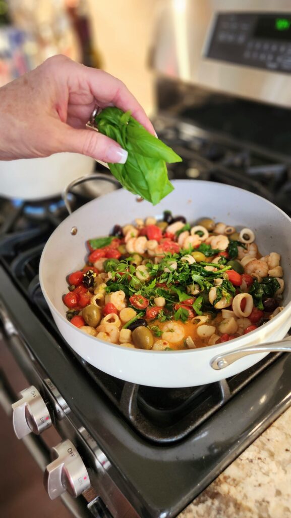 tearing fresh basil over finished mediterranean seafood blend skillet