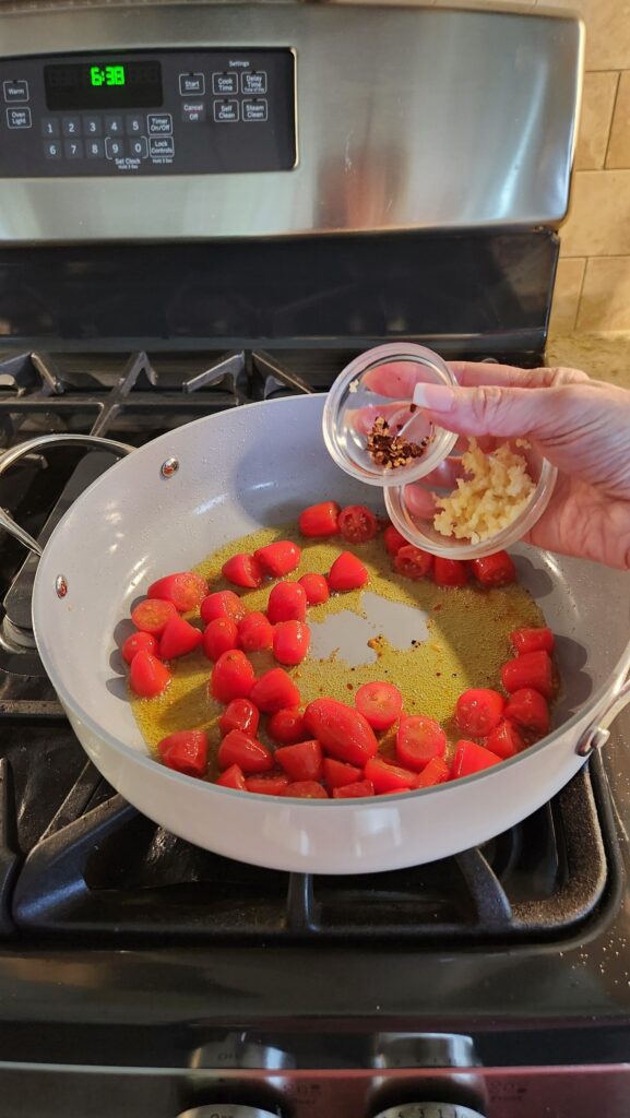 adding minced garlic and red pepper flakes to cherry tomatoes in skillet