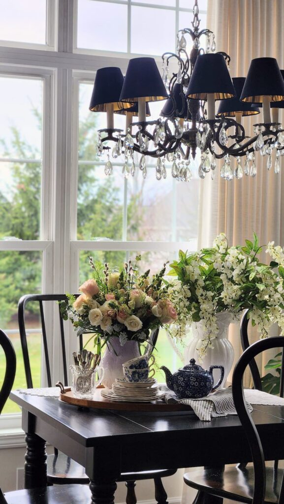 How to arrange spring flowers in a vintage vase breakfast room wide shot crystal chandelier plate wall pink roses white wisteria French country home decor