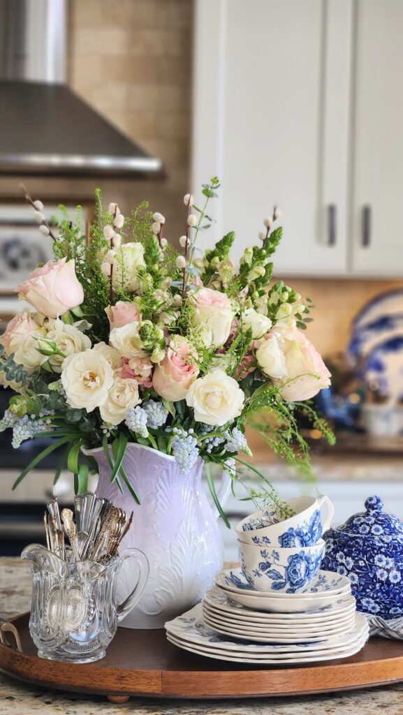 How to arrange spring flowers in a vintage vase kitchen counter lavender pitcher pink cream roses blue and white china teacups blue ginger jar background