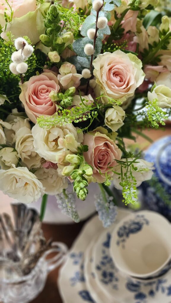 How to arrange spring flowers in a vintage vase breakfast room chandelier overhead pink roses lavender pitcher white wisteria white pitcher blue and white china