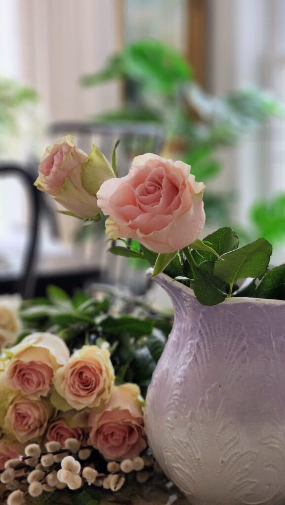 How to arrange spring flowers in a vintage vase single pink rose bud in lavender pitcher fresh flowers laid out counter first step floral arrangement