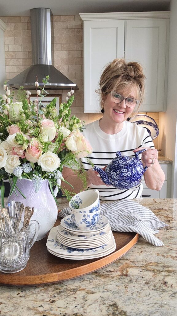 Susan of Hen and Horse Design arranging spring flowers in a vintage vase kitchen counter lavender pitcher pink roses blue and white chinoiserie teapot