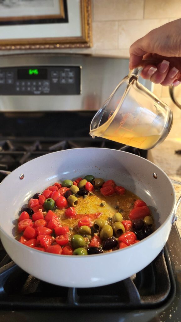 pouring white wine into skillet to build mediterranean seafood sauce