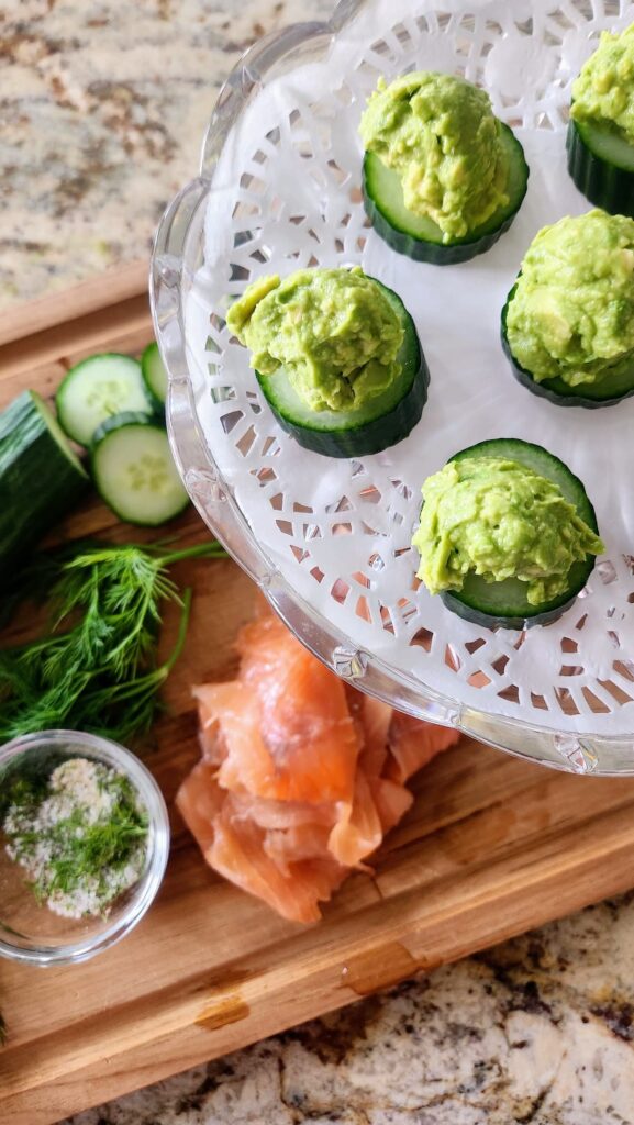 cucumber rounds topped with avocado mash on crystal cake stand ready to assemble