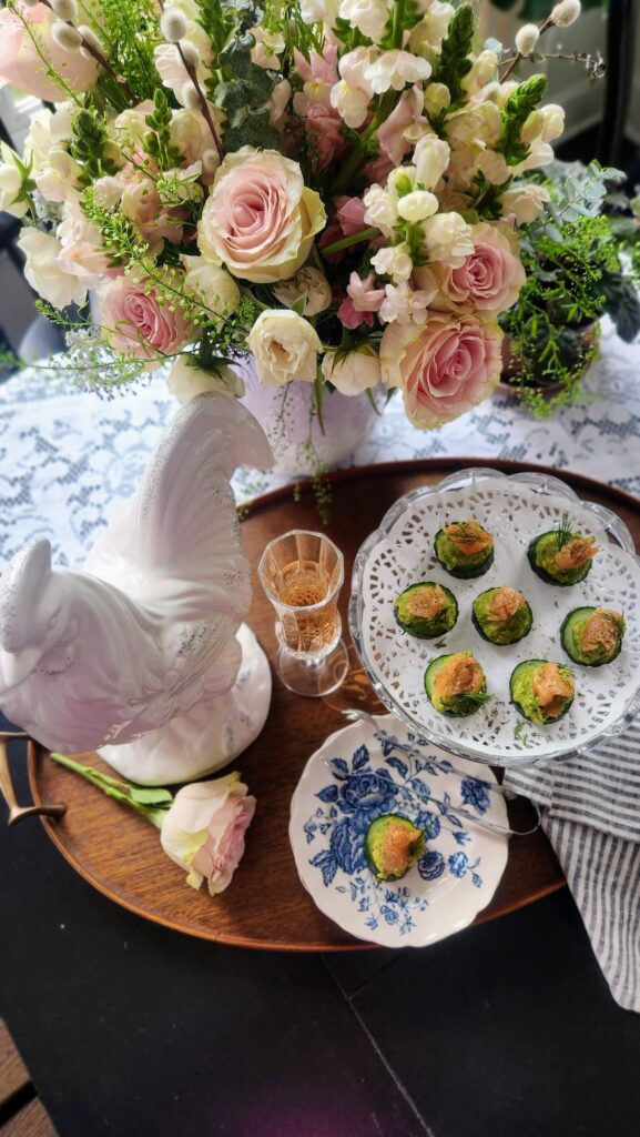 overhead view of smoked salmon cucumber bites on crystal cake stand with spring flower arrangement