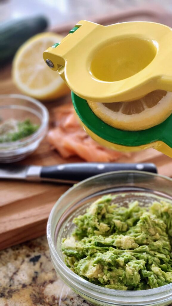 squeezing fresh lemon juice into mashed avocado for smoked salmon cucumber bites appetizer