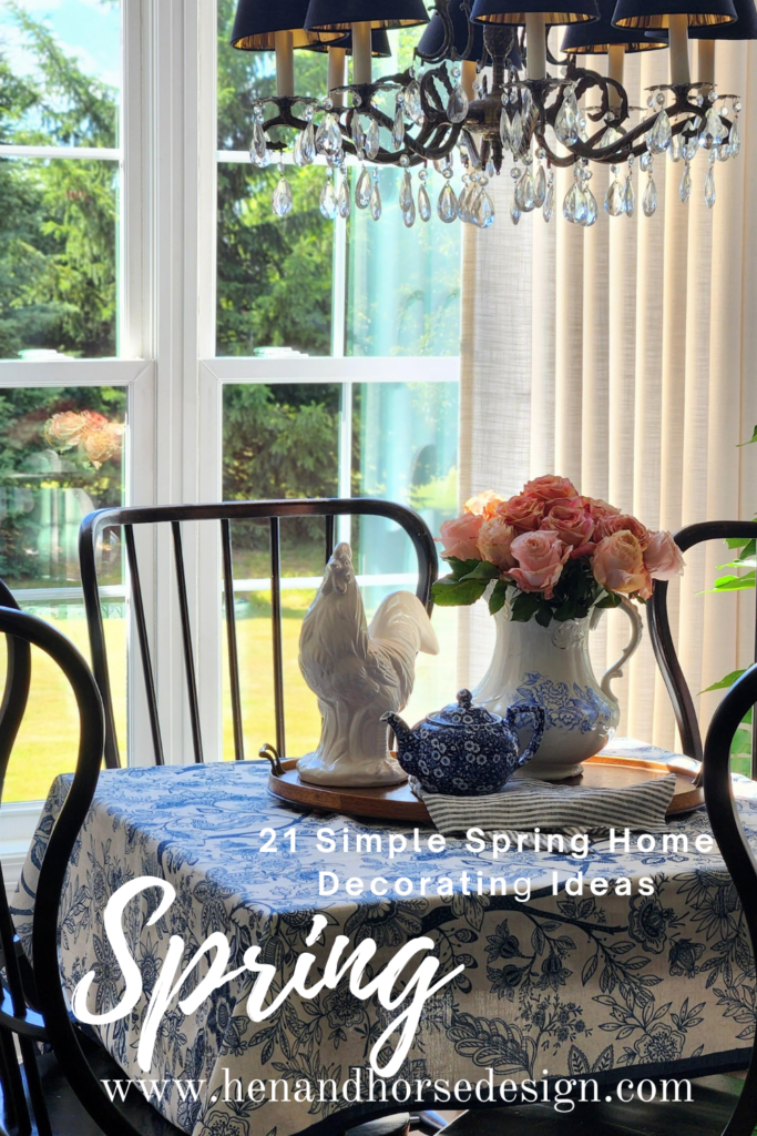 French country dining room table styled with a blue and white toile tablecloth, peach garden roses in a white ironstone pitcher, white ceramic rooster, blue teapot, and antique bronze crystal chandelier — simple spring home decorating ideas