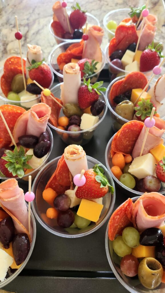 Individual charcuterie appetizer cups with cured meats cheese fruit and olives on serving tray