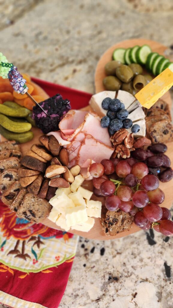 Small round charcuterie board with sliced ham brie cheese grapes blueberries crackers and mini pickles